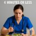 Nurse in blue scrubs eating a salad quickly during a short break, with an apple and water bottle on the table.
